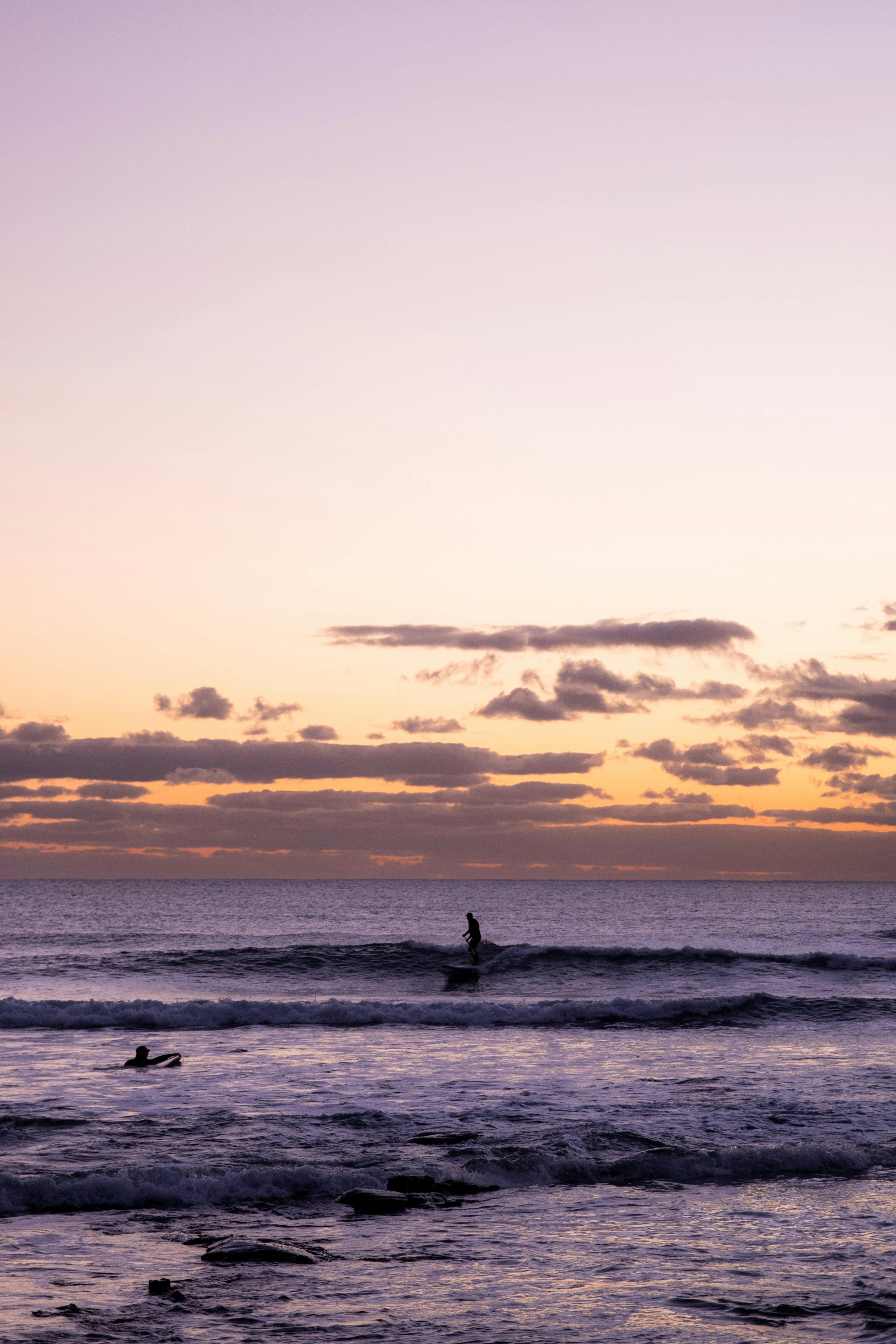 Silhouetted surfers ride the waves during a stunning purple and gold sunrise at Sunshine Coast, Australia.