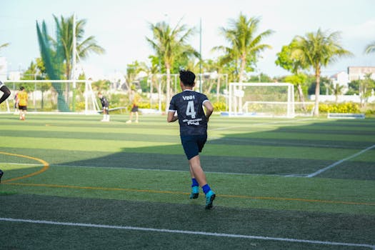 A teenager in sportswear running on a sunny outdoor soccer field during a game.