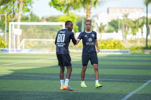 Two soccer players greet each other during practice on a sunny outdoor field.