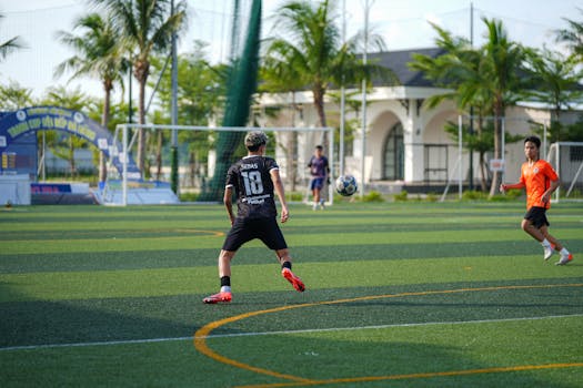 Soccer players compete on a lush green field under clear skies in daytime.