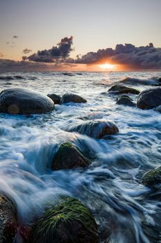 Stunning ocean sunset with waves crashing over mossy rocks.