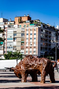 A modern bull sculpture on a busy street in Madrid, Spain against an urban backdrop.