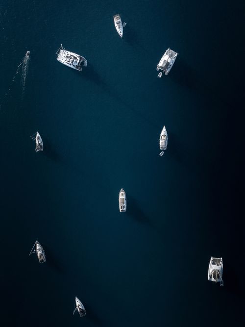 Free Aerial shot of boats scattered on dark blue ocean waters, showcasing tranquility. Stock Photo