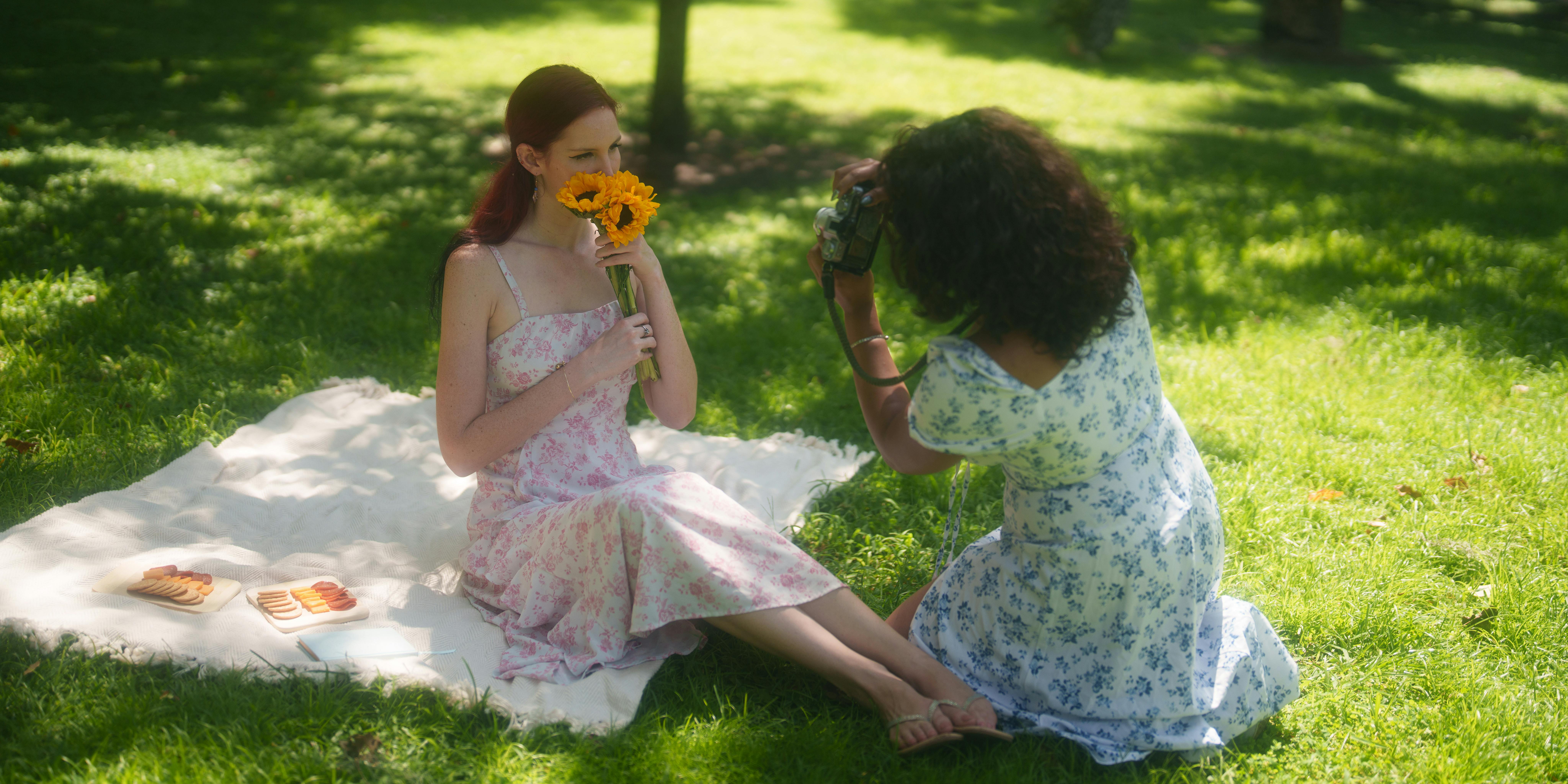 Two women enjoy a lively summer picnic with sunflowers and cookies.