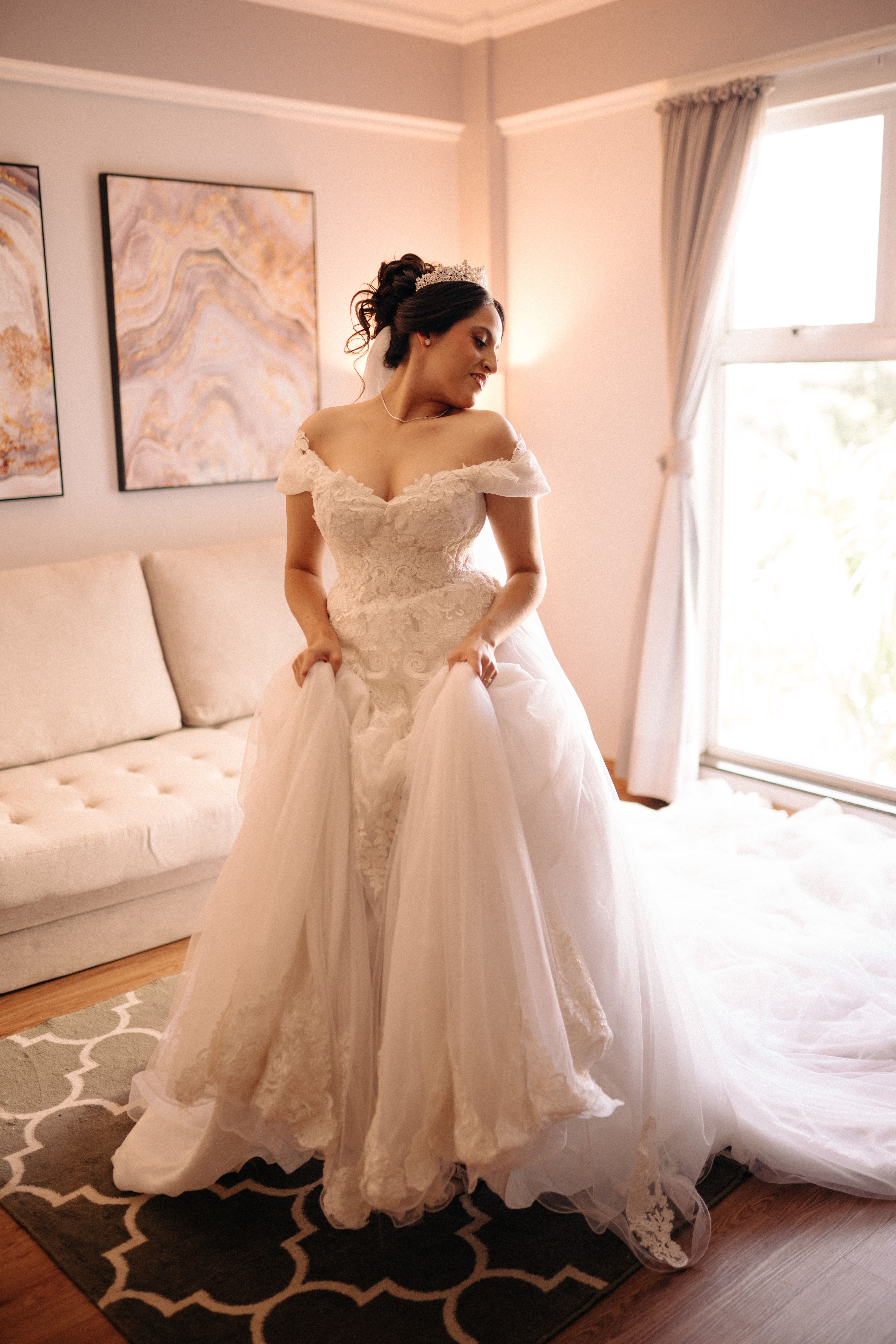 A bride in a luxurious wedding gown stands gracefully in a well-lit room, embodying elegance and anticipation.