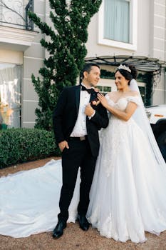 Bride and groom in elegant attire pose outdoors for a wedding photo.
