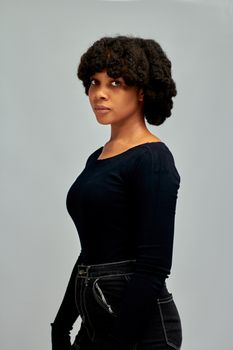 Stylish studio portrait of a young woman in black with natural curly hair against gray background.