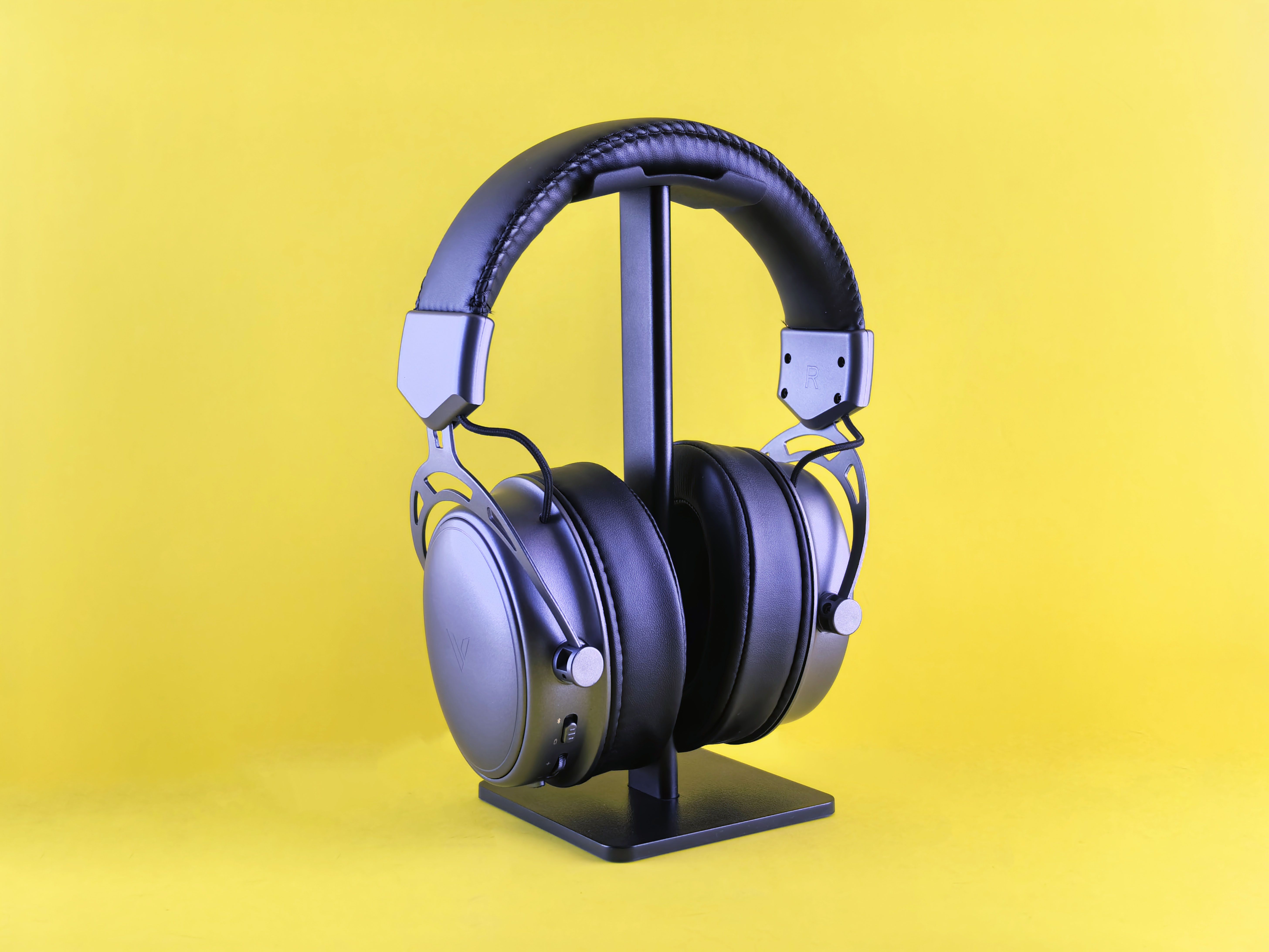 Sleek black headphones on a stand against a vivid yellow backdrop, highlighting modern audio design.