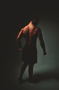 Athletic male silhouette posing confidently in moody studio lighting, showcasing muscle definition and strength.