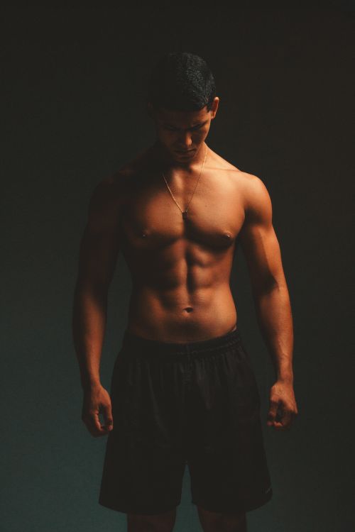 Free Muscular male athlete posing shirtless in dramatic lighting, showcasing fitness and strength. Stock Photo