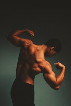 Back angled view of a muscular man flexing his arms, emphasizing strength and physique.