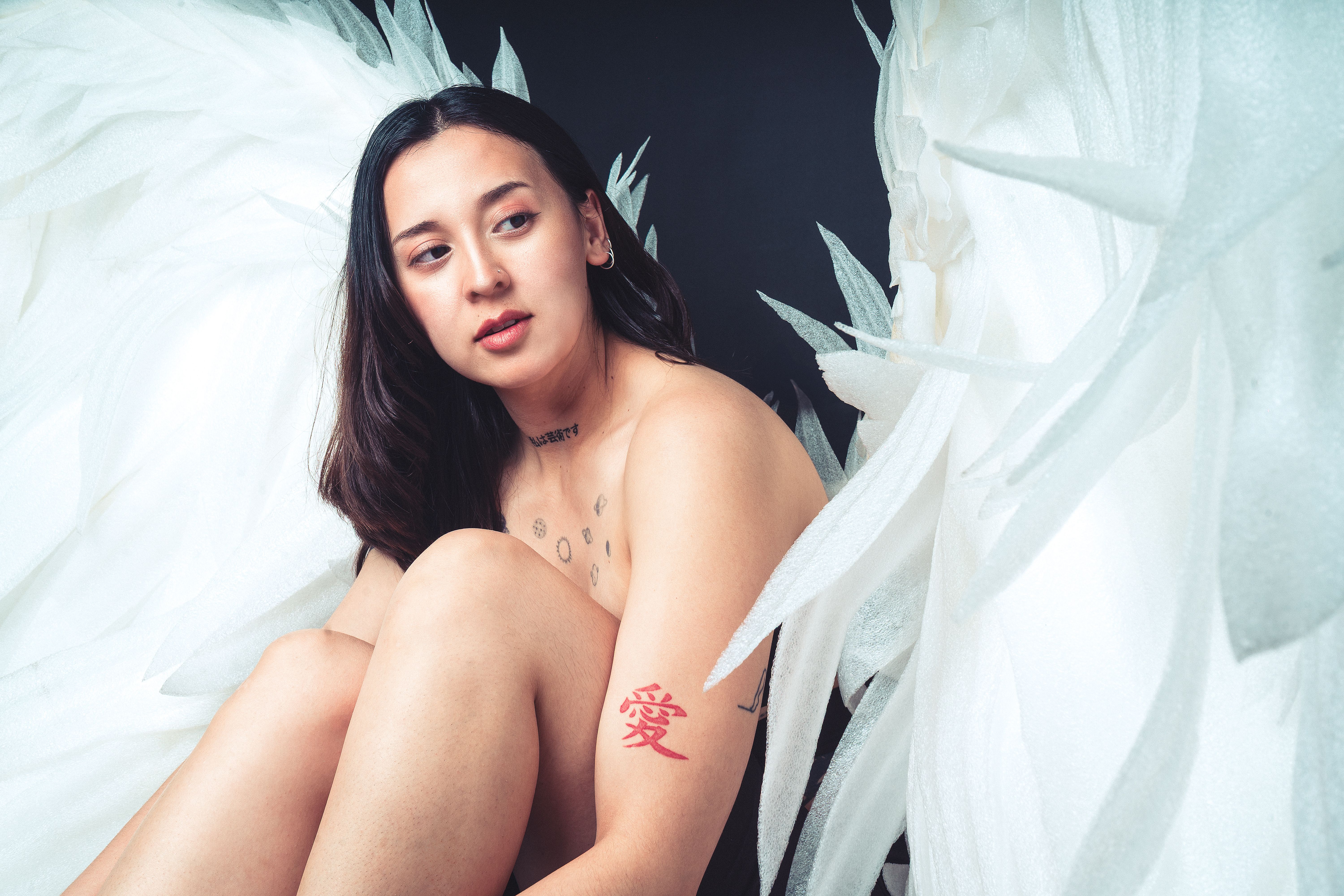 Artistic portrait of a woman with tattoos surrounded by angelic white wings, evoking a serene and ethereal mood.