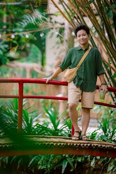 Adult standing on a small bridge in a vibrant, lush garden setting, holding a drink.