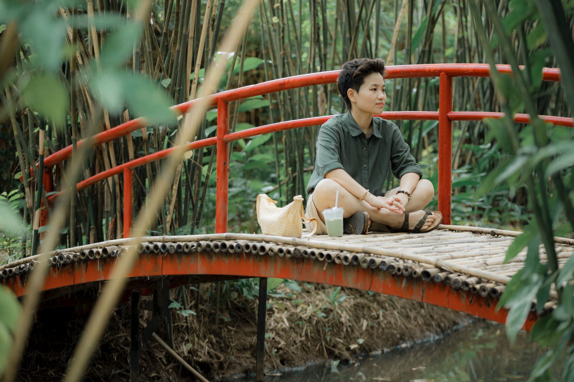 A person sitting on a bamboo bridge surrounded by lush greenery in a tropical garden setting.