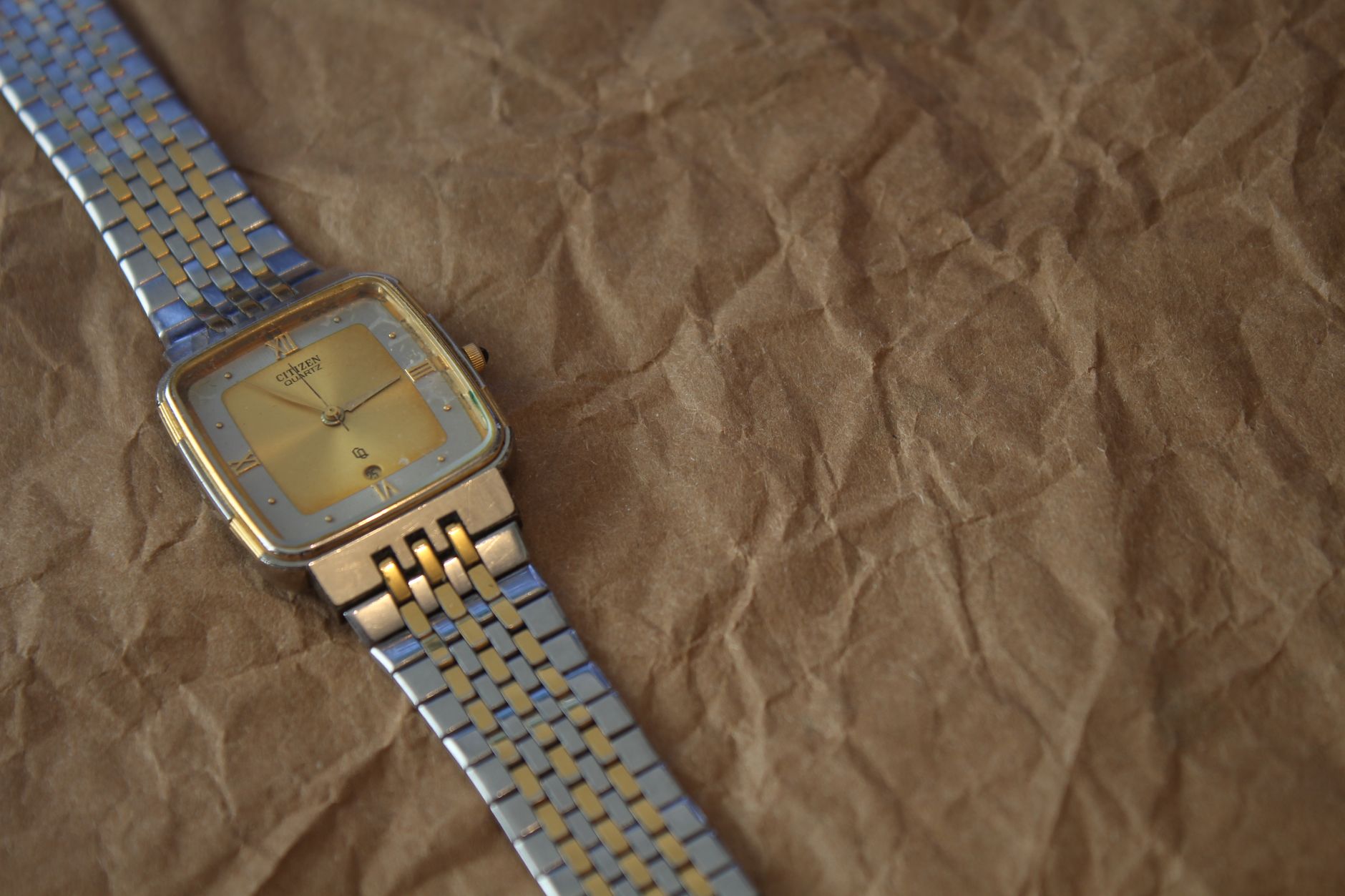 Un elegante reloj de pulsera dorado y plateado sobre papel arrugado, simbolizando el paso del tiempo y la urgencia