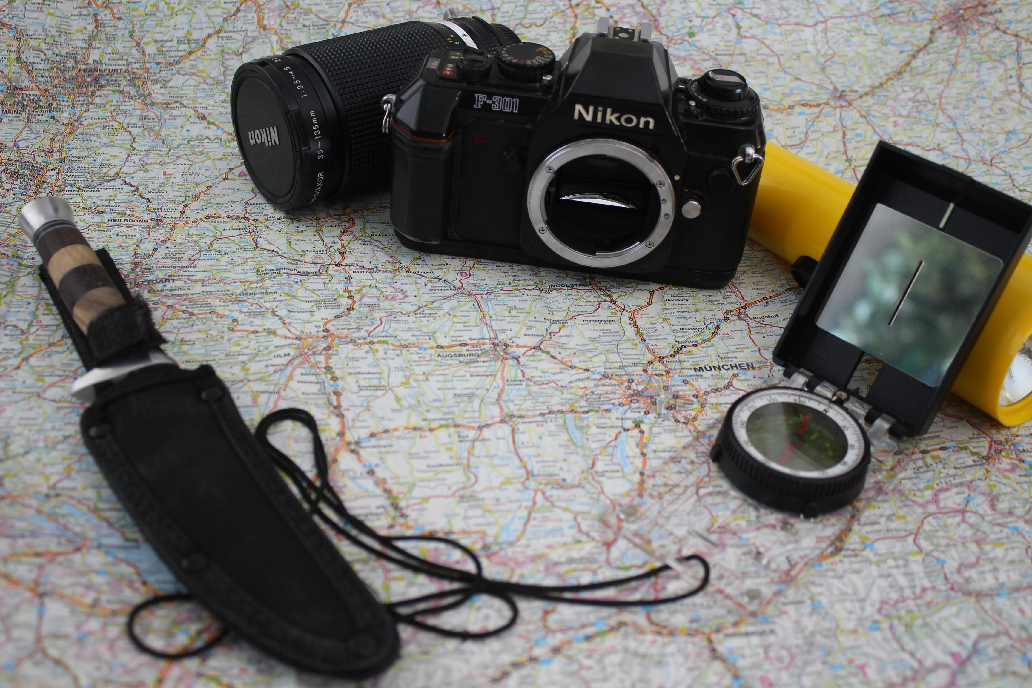 A nostalgic journey with a Nikon camera, compass, knife, and flashlight on a detailed map.
