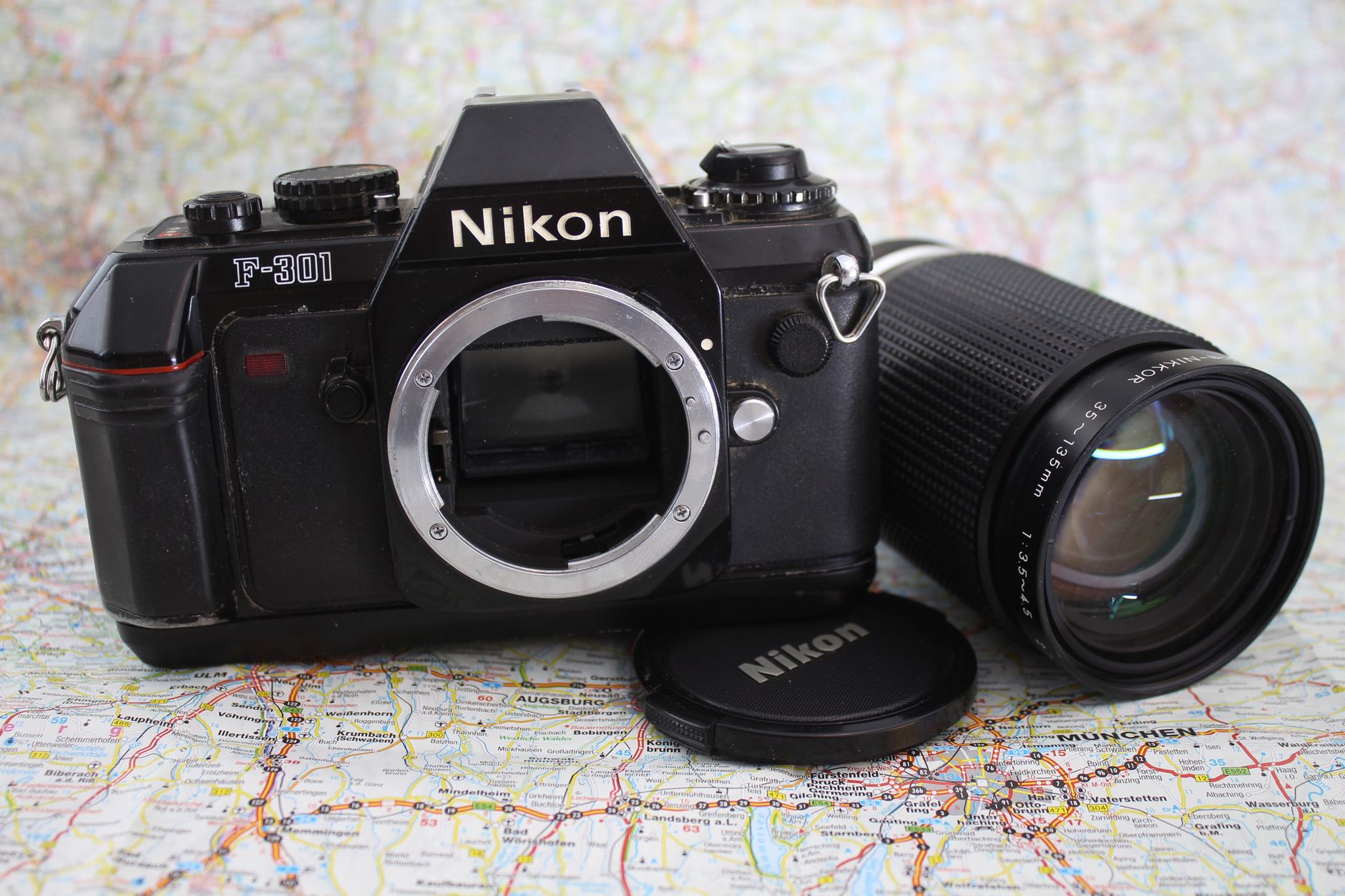 Classic Nikon F-301 camera with lens displayed on world map, evokes travel and photography nostalgia.