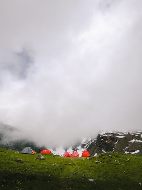 Free Red tents on a green hill under a misty mountain sky, capturing nature's tranquility. Stock Photo