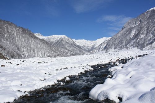 Free Scenic winter view of snow-covered mountains and flowing river in a tranquil valley. Stock Photo