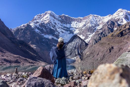 Woman in blue gown with shawl near snowy mountain and lake. Serene and scenic.