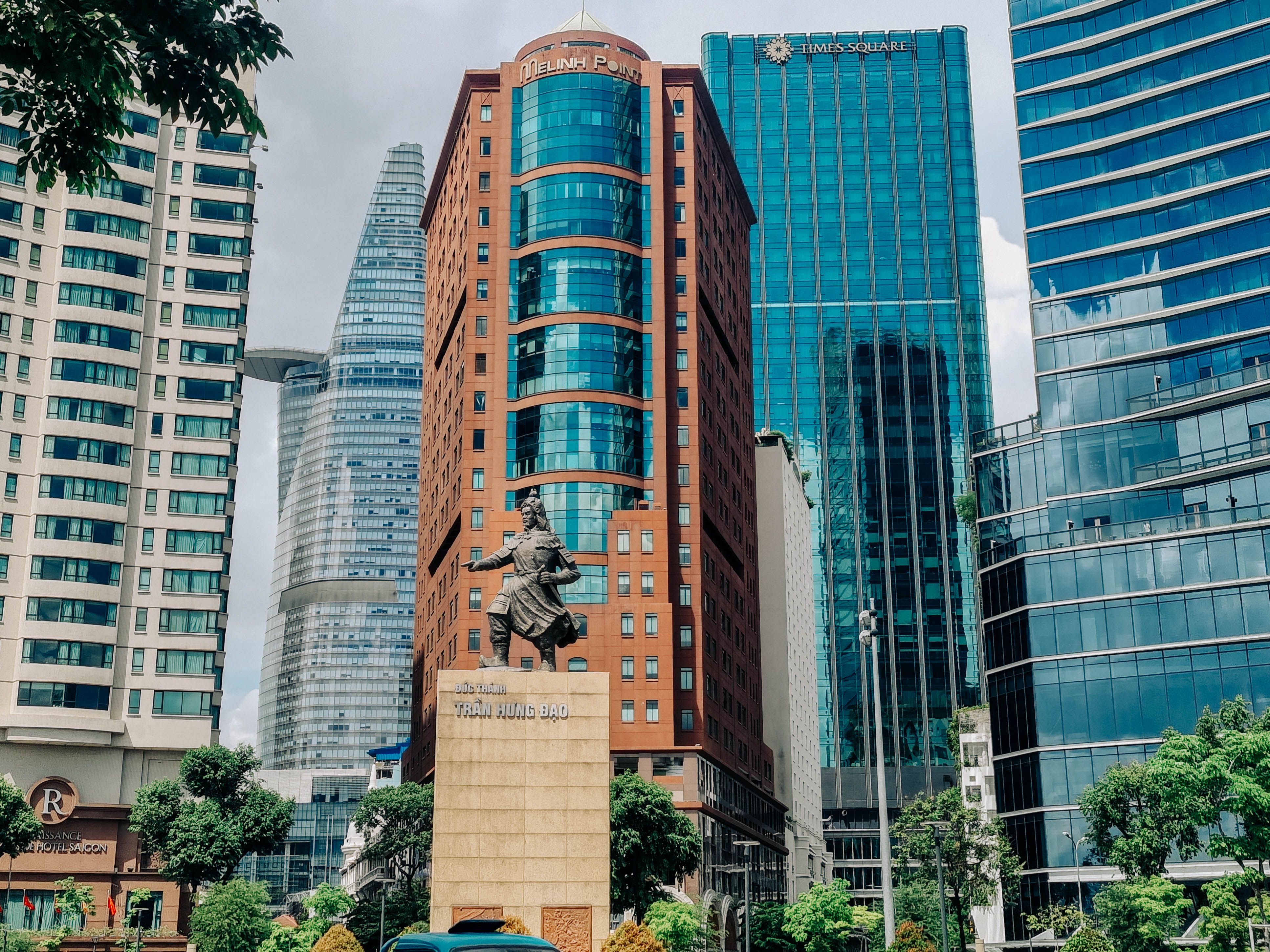 Dynamic urban scene featuring skyscrapers and a historical statue in Ho Chi Minh City, Vietnam.