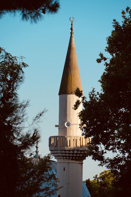 Free A soaring mosque minaret stands amidst lush trees under a clear blue sky. Stock Photo