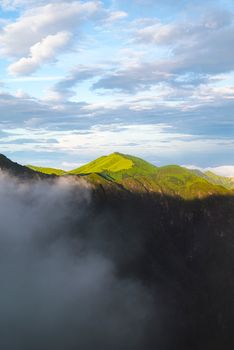 Scenic view of lush mountain peaks emerging through misty clouds under a vibrant sky.