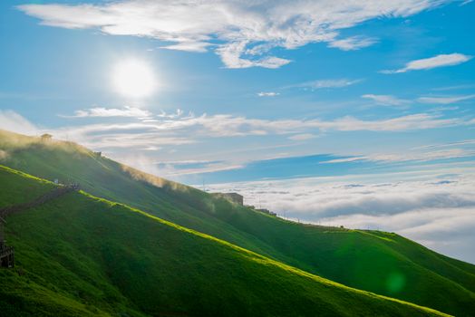 Sunrise over vibrant green hills with clouds and mist in a serene mountain landscape.