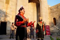 A group of actors perform in traditional Azerbaijani costumes outside a historic building.