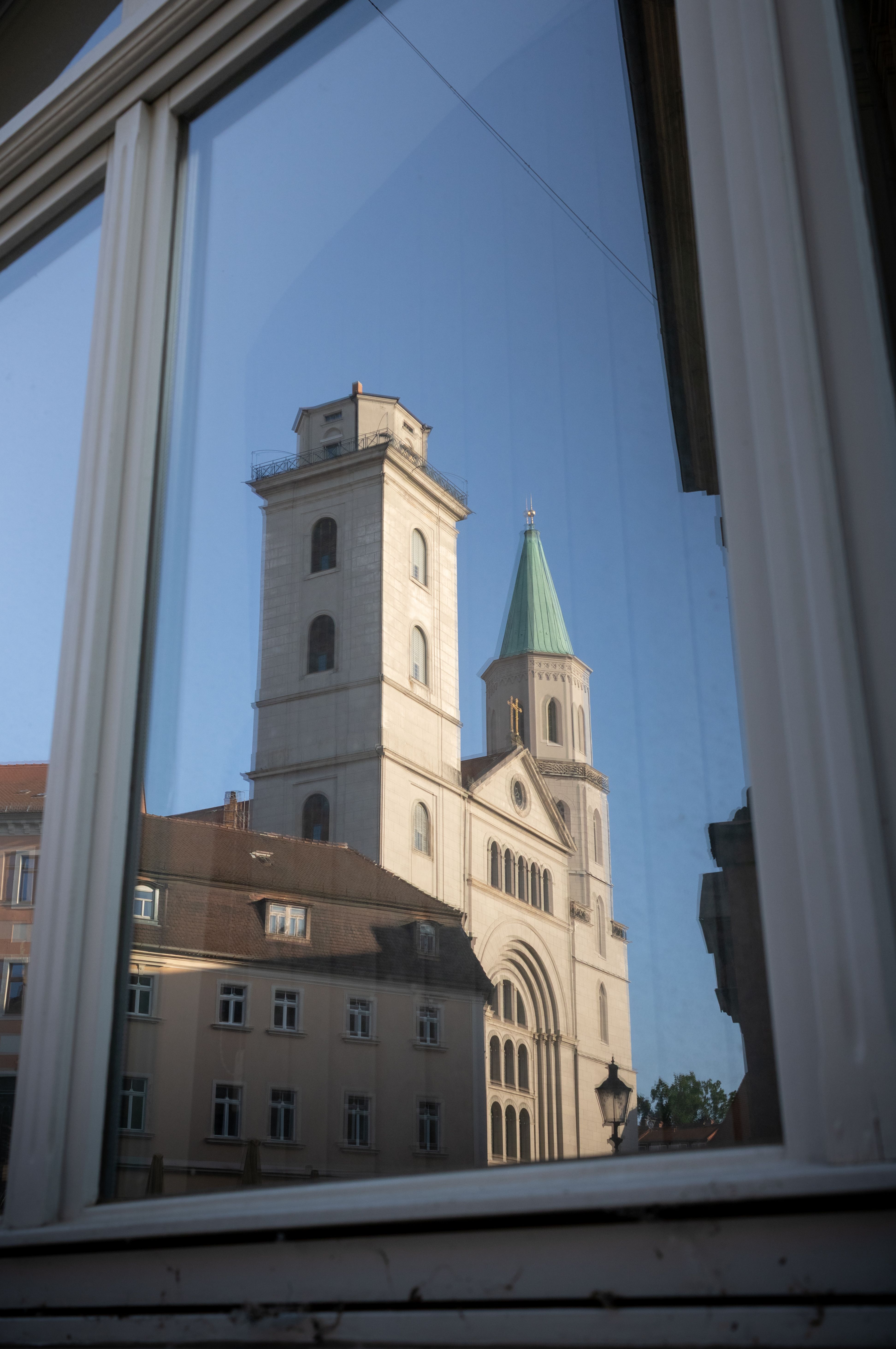 A church with a green spire reflecting in a window in Zittau, Germany.