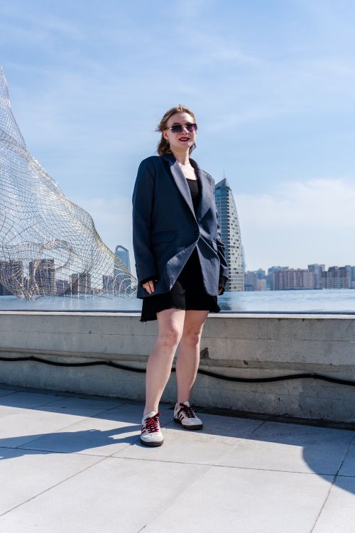 Free Stylish person in oversized blazer and dress near modern city waterfront on a sunny day. Stock Photo