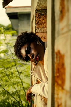 Elegant portrait of a black woman in sunglasses leaning out of a rustic window.