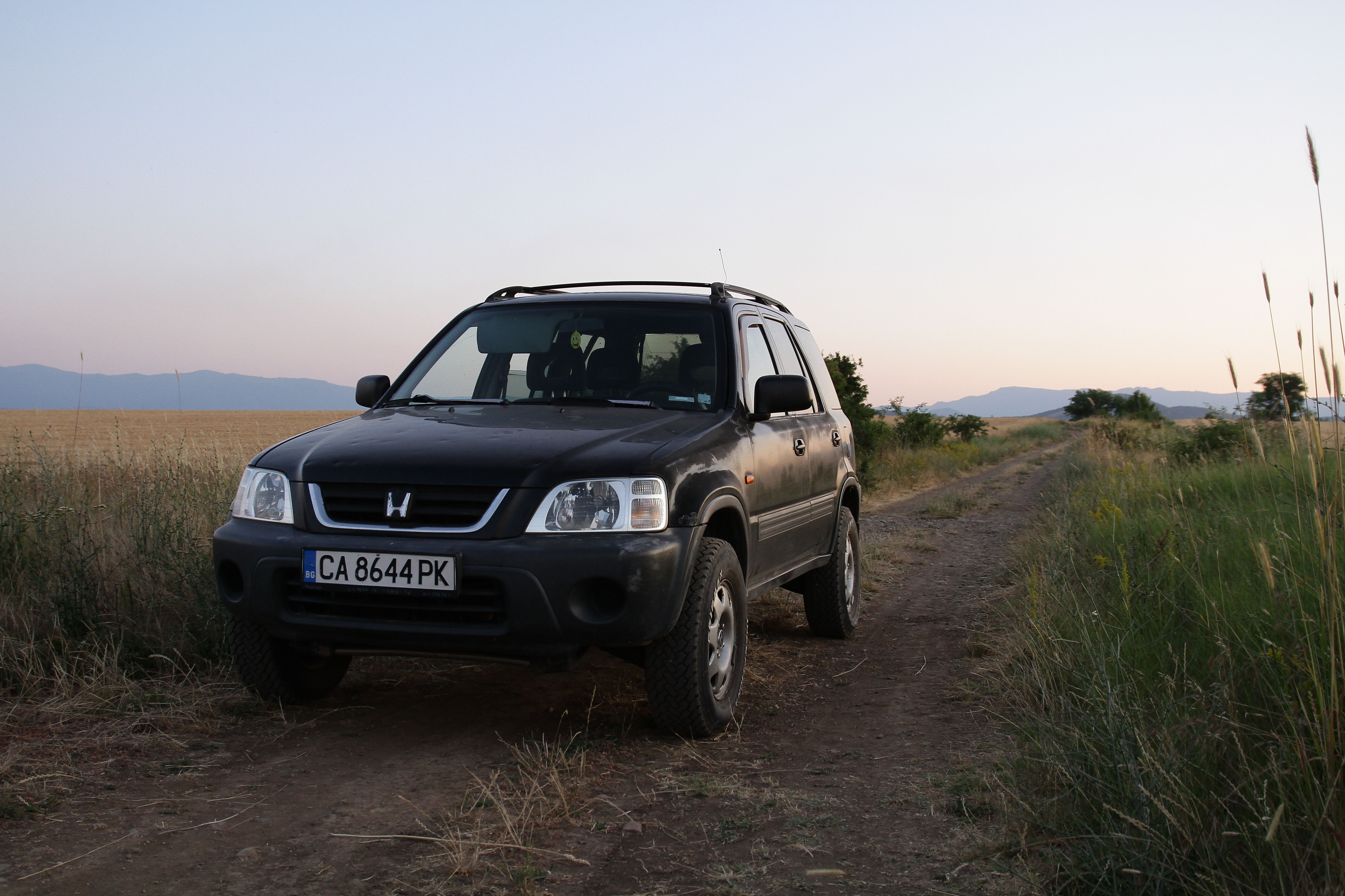 Black SUV on a dirt road surrounded by fields at sunset, capturing a serene rural landscape.