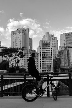 Black and white photo of a cyclist resting by a cityscape under an open sky.