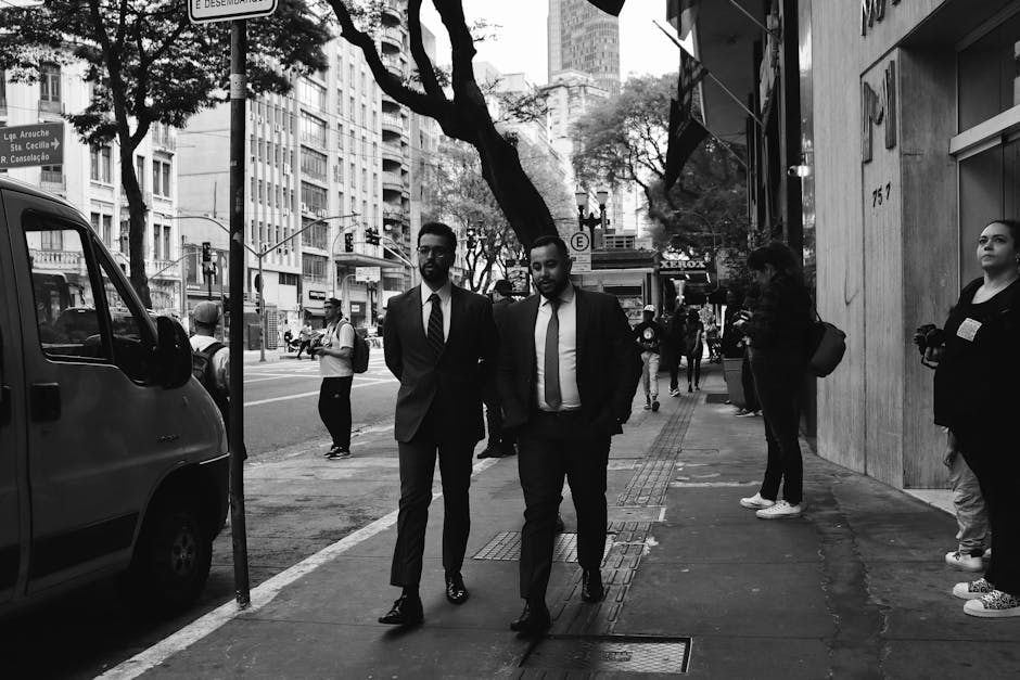 Two businessmen in suits walk on a busy urban street with skyscrapers.