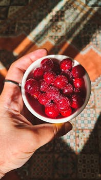 Hand holding a bowl filled with fresh bright red cherries on patterned tile background.