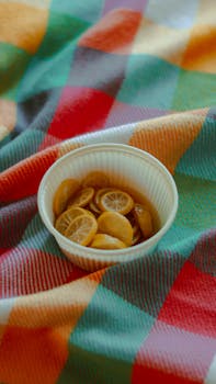 A small white bowl of sliced kumquats rests on a vibrant checkered blanket, offering a fresh and colorful composition.
