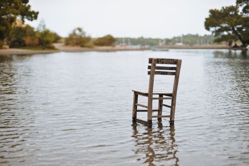 Free A solitary wooden chair stands in a calm lake surrounded by nature, evoking solitude and peace. Stock Photo