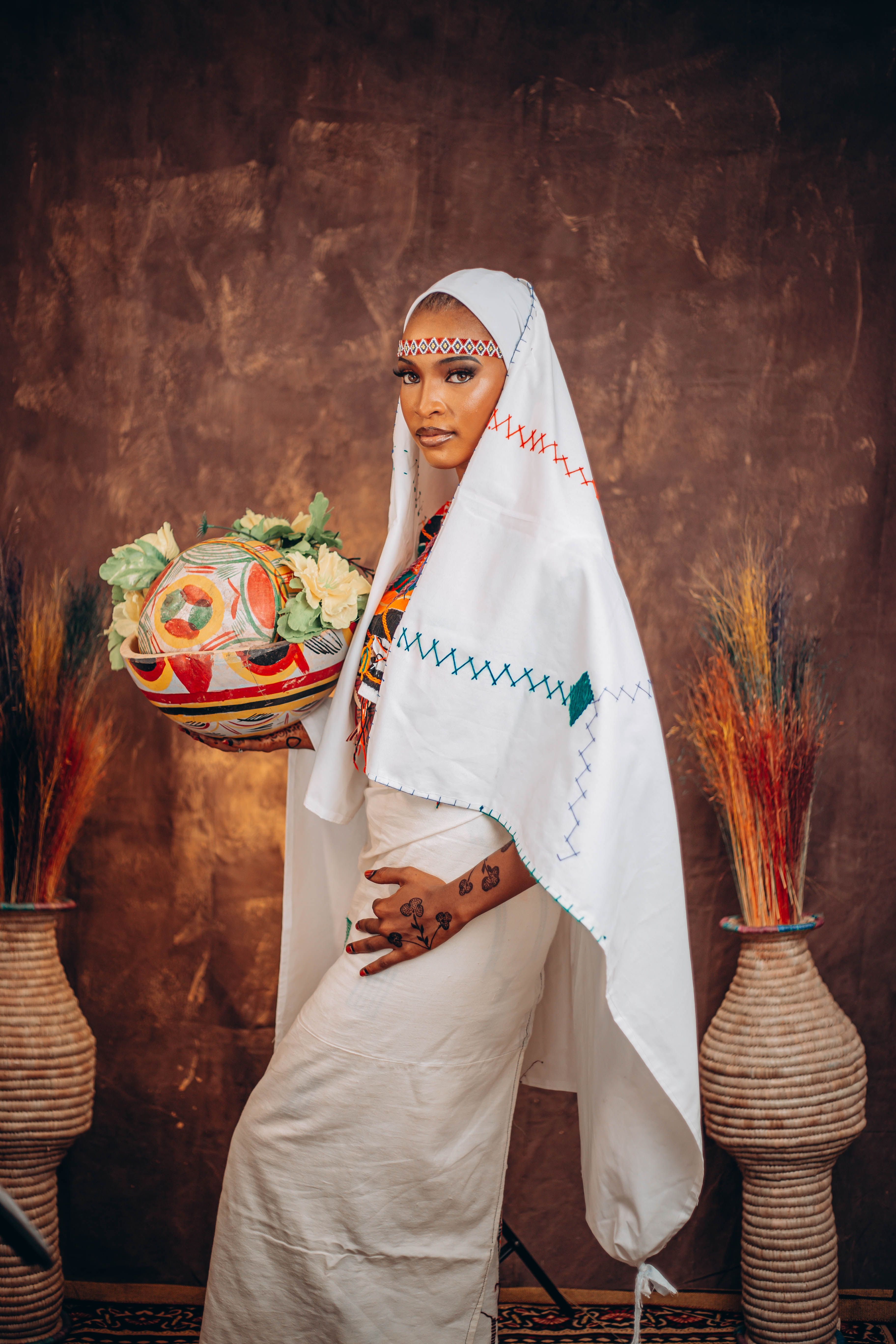 Woman in cultural African clothing holding a basket of fruits against a rustic background.