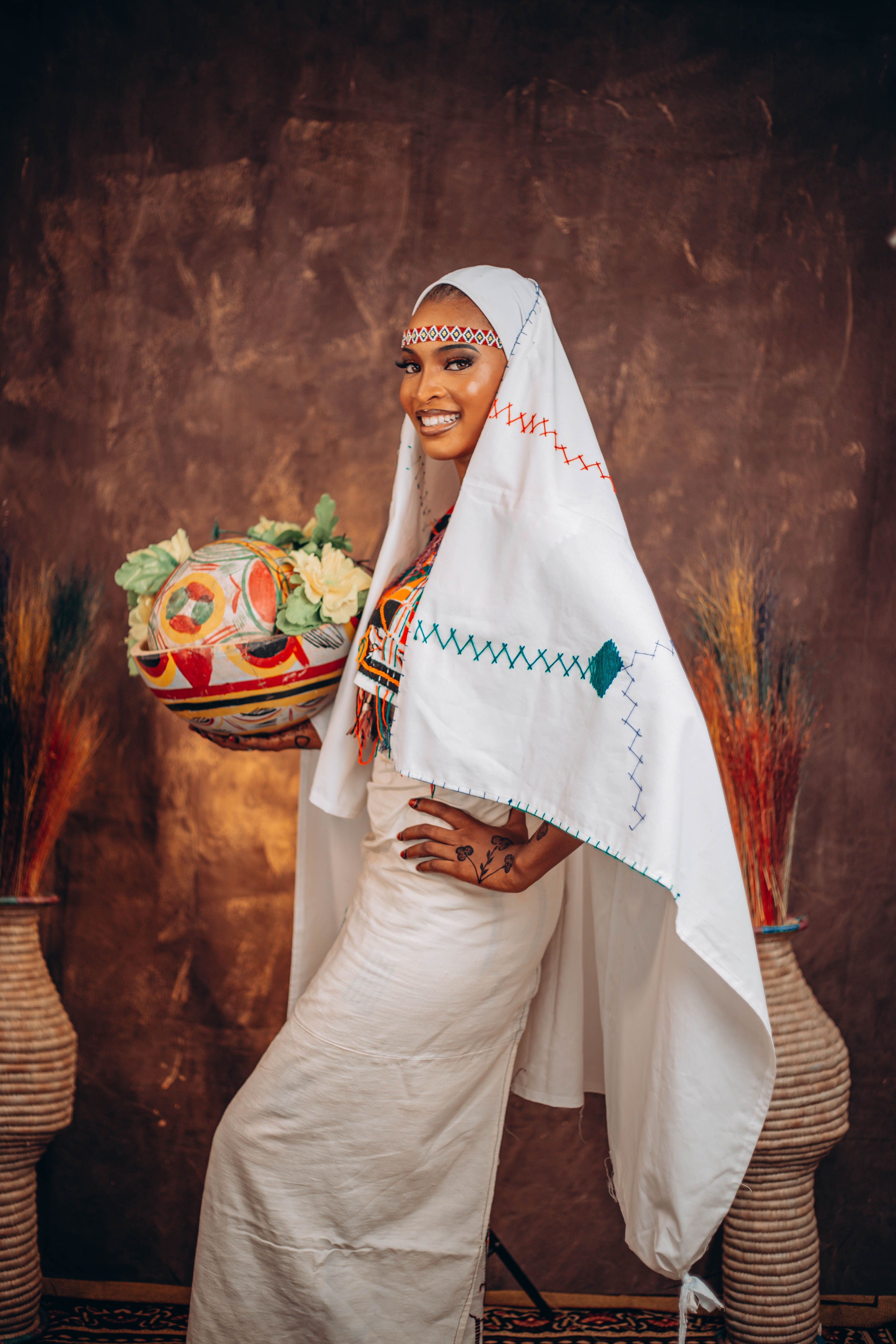 Smiling woman in colorful traditional African dress holding decorative basket.
