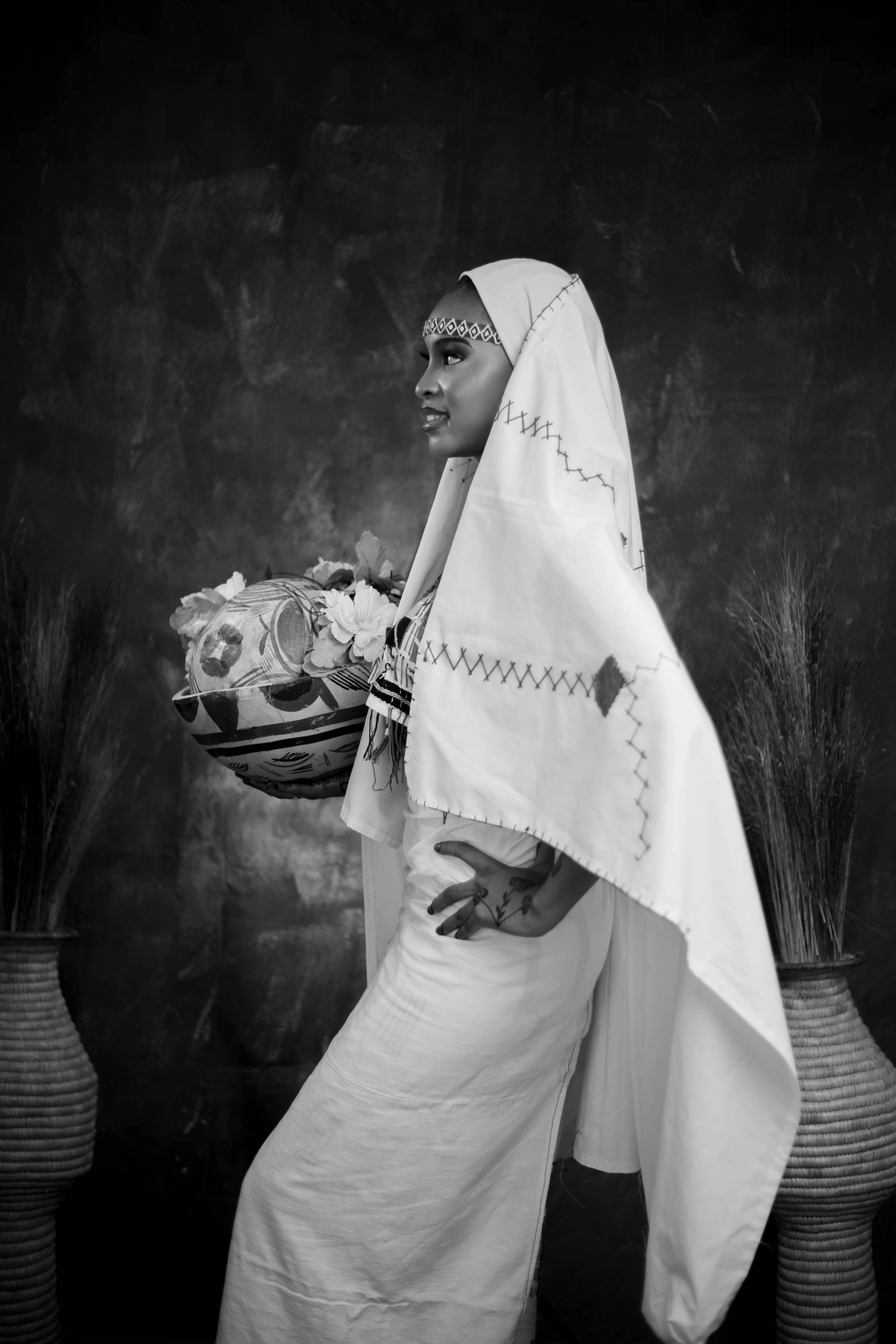 Black and white photo of a woman in traditional attire holding a decorated pot.