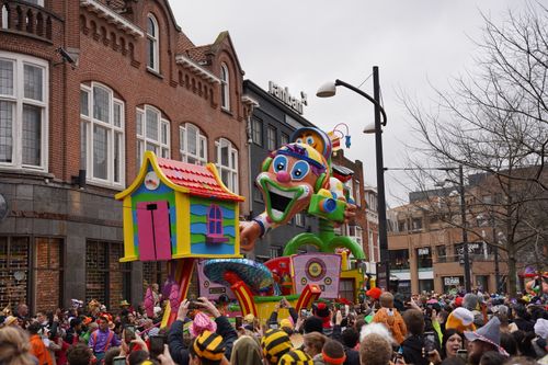 Free Lively street festival in Holland featuring colorful floats and a joyful crowd under cloudy skies. Stock Photo