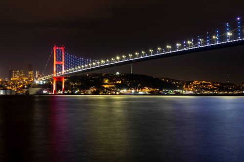 Free The Bosphorus Bridge shines brightly over Istanbul's cityscape, reflecting in the tranquil waters at night. Stock Photo