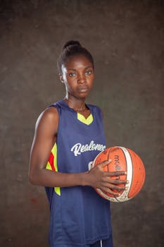 Focused young female basketball player holding a ball in a studio setting.