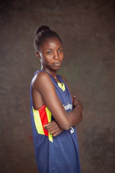 Young African basketball player confidently posing indoors with a neutral backdrop.
