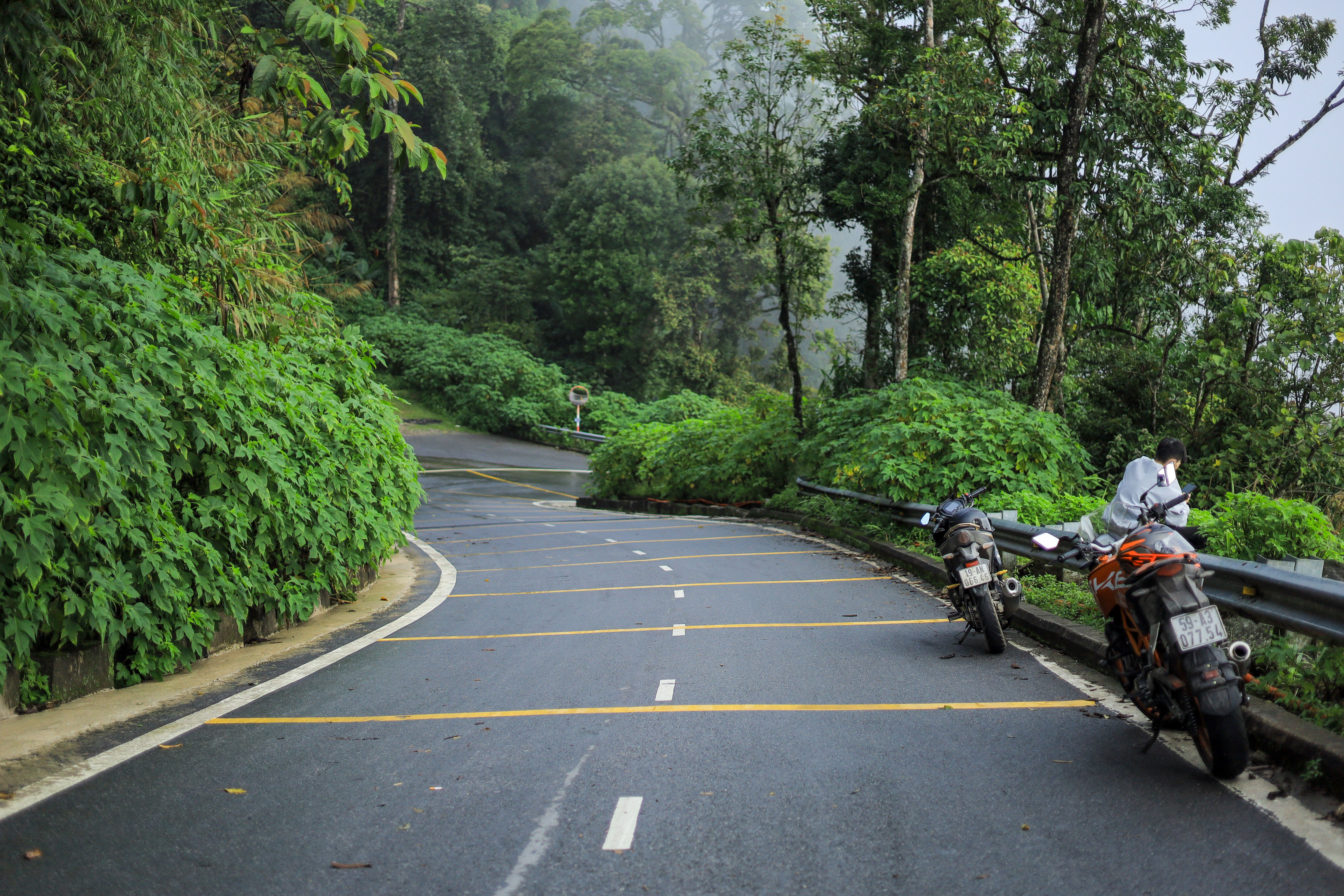 Curvy mountain road in Vietnam with two parked motorcycles surrounded by lush greenery.