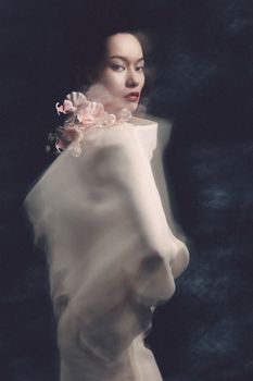 Portrait of a woman wrapped in ethereal fabric with flowers, capturing a dreamy, artistic mood.