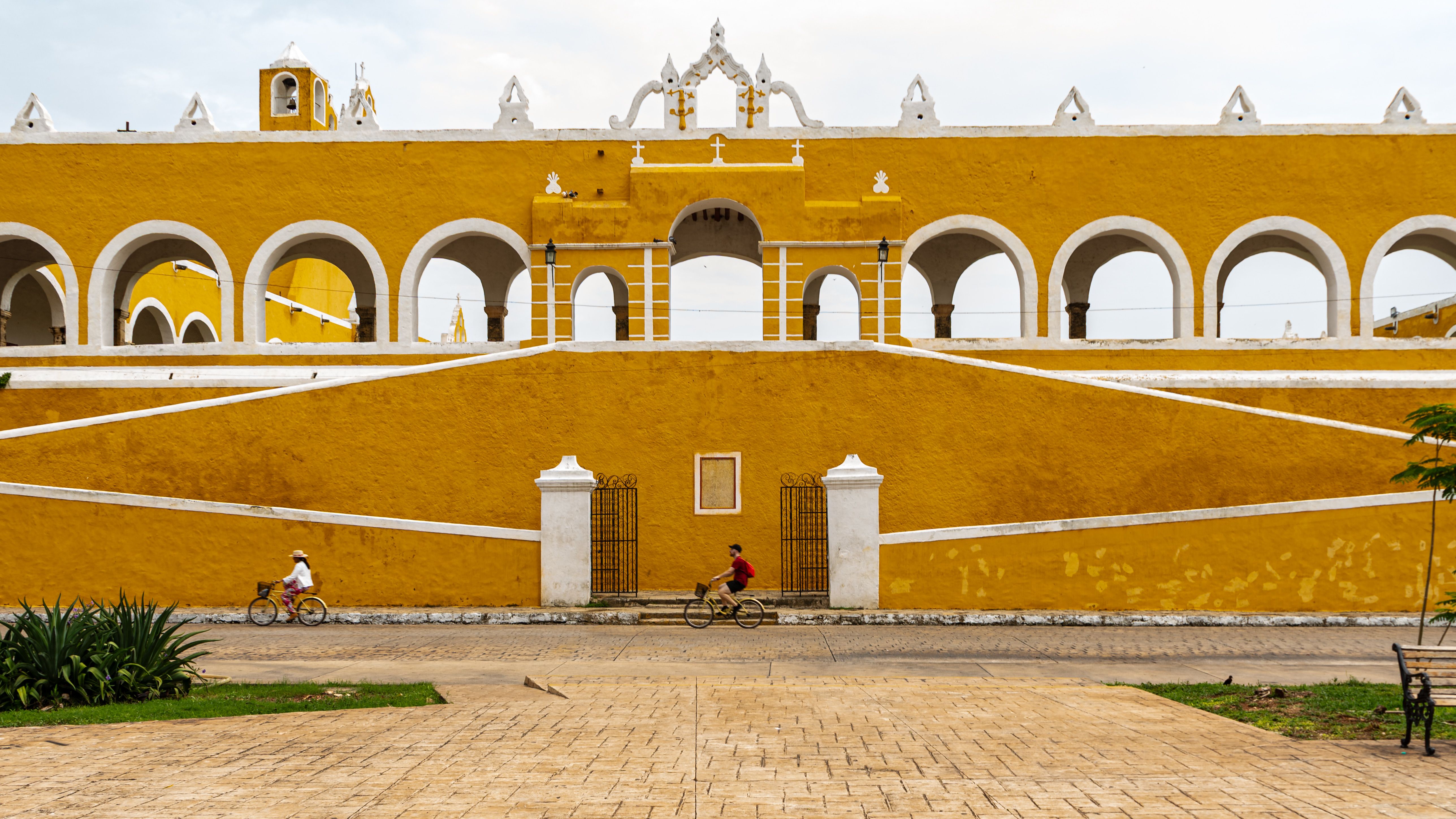 Vibrant yellow colonial-style building with cyclists, Izamal, Mexico.