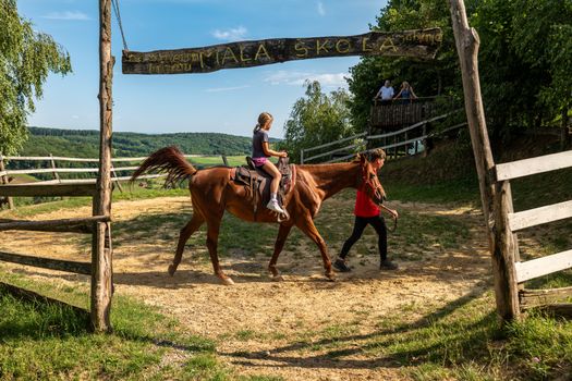 A child rides a horse led by an instructor at Mala Skola in scenic Croatian countryside.