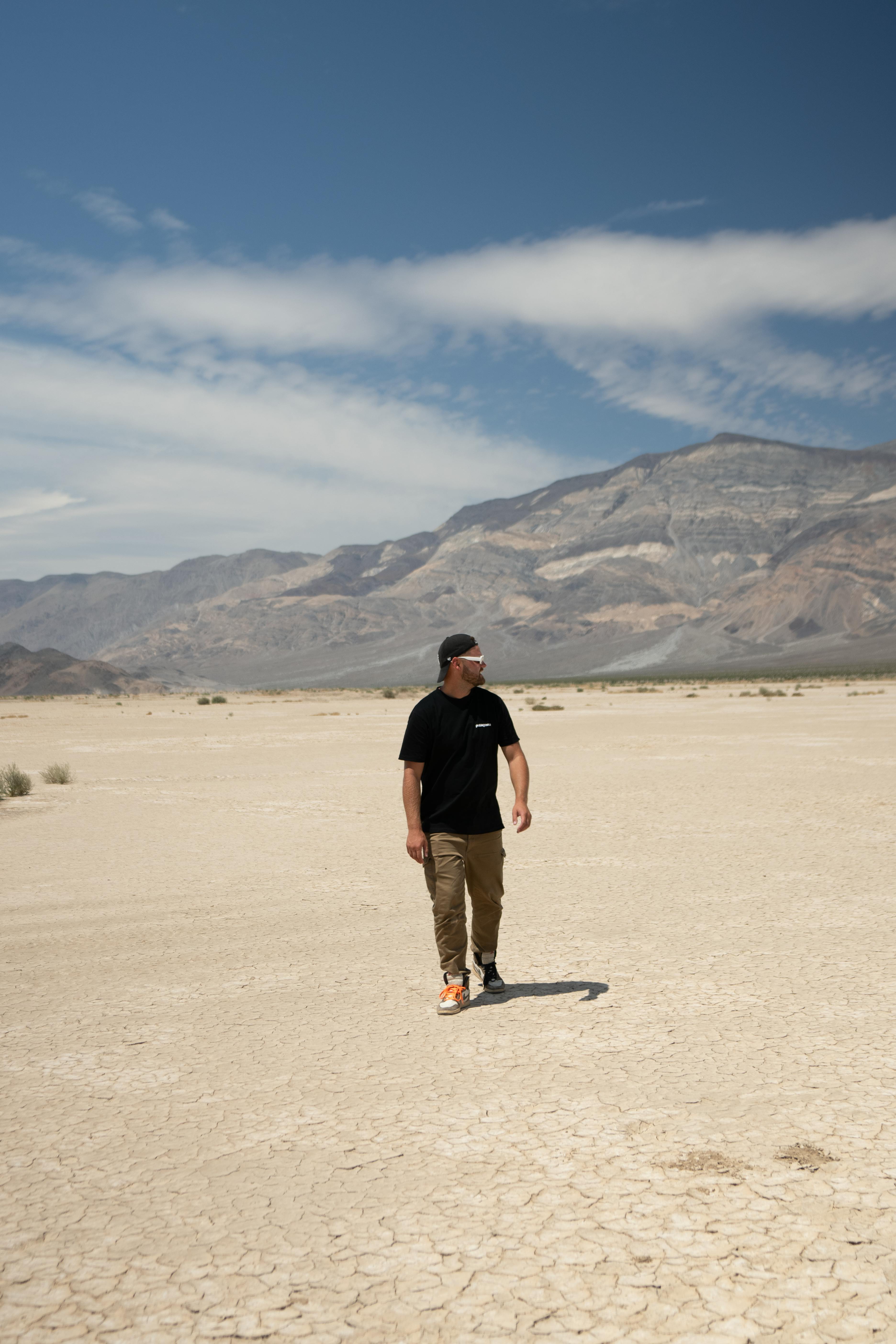 бесплатная Одинокий мужчина идет по бескрайней пустыне в Калифорнии под ясным голубым небом. Стоковое фото